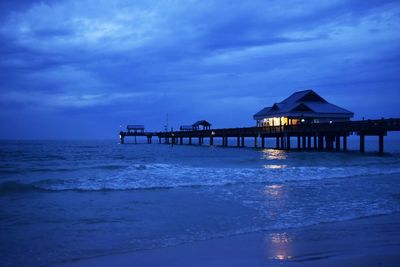 Pier on beach against cloudy sky