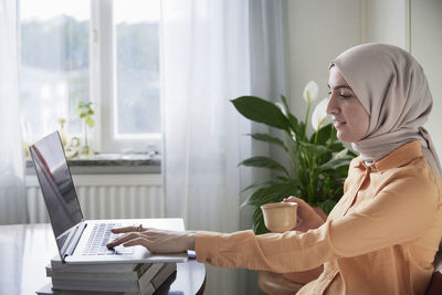 Smiling woman with hijab working from home using laptop