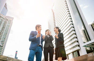 Low angle view of happy business colleagues talking while standing against buildings in city