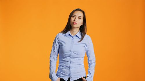 Portrait of young woman standing against yellow background