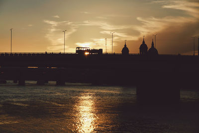 Silhouette bridges over river against sky during sunset