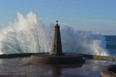 Wave splashing on lighthouse against clear sky