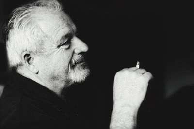 Close-up of man smoking cigarette against black background