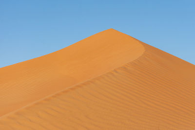 Sand dunes in desert against clear blue sky