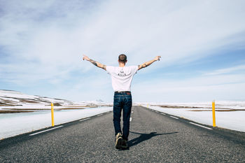 REAR VIEW OF MAN WITH ARMS OUTSTRETCHED STANDING ON ROAD