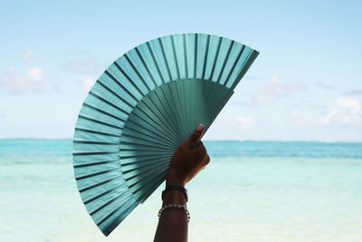 Woman holding fan by sea against sky
