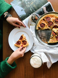 Cropped image of hands holding pizza in plate on table