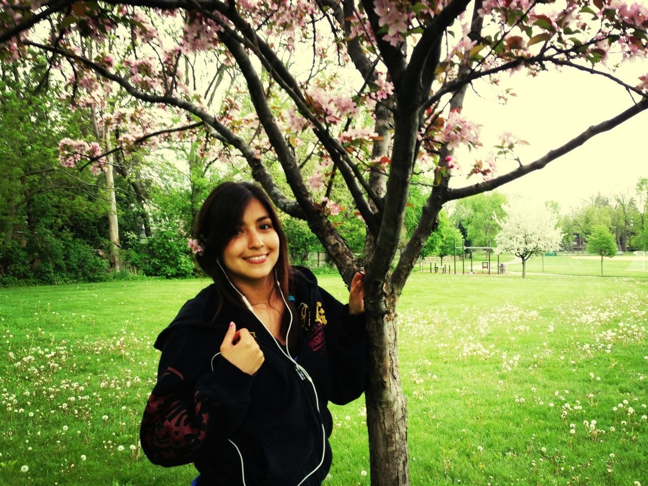 tree, lifestyles, leisure activity, young adult, person, grass, casual clothing, young women, looking at camera, smiling, park - man made space, portrait, front view, green color, growth, standing, long hair, nature