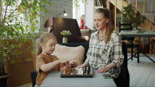 Teacher teaching chess to daughter at home