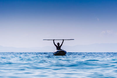 Woman holding oar moving in boat on sea against sky