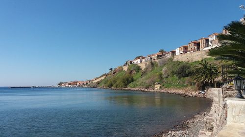 Scenic view of sea by buildings against clear blue sky