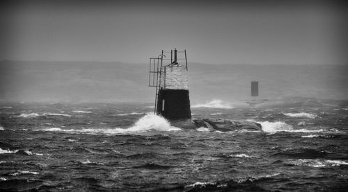 Lighthouse by sea against clear sky