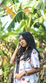 Thoughtful young woman standing against banana trees