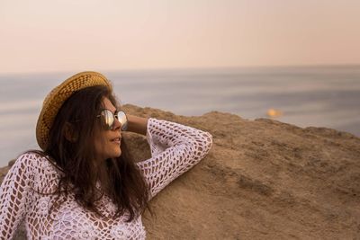 Woman relaxing at beach against sky during sunset