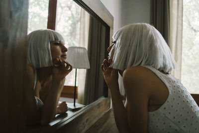 Sad woman looking her reflection in mirror while standing by dressing table at home