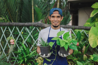 Portrait of smiling botanist holding plant at shop