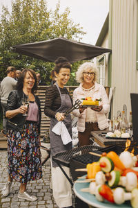 Happy elderly female friends preparing dinner on barbecue at back yard