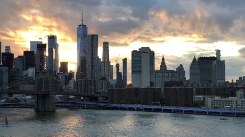 Modern buildings by river against sky during sunset