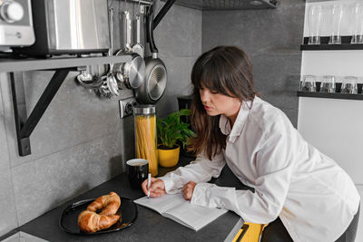 Young attractive woman in white shirt writing in notebook on kitchen counter. portrait of an attract