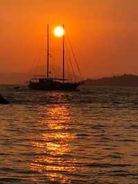 Silhouette sailboat sailing on sea against orange sky during sunset