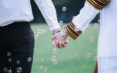 Midsection of couple holding hands amidst bubbles