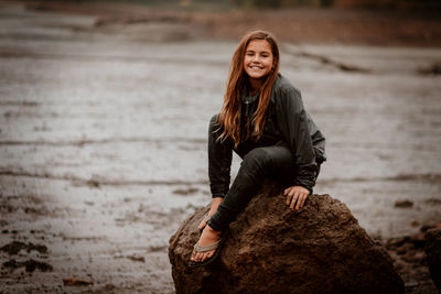 Portrait of smiling girl sitting on rock 