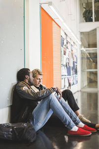 Young man sitting with male friend in corridor of university