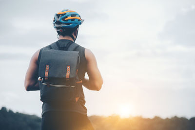 Rear view of man with backpack standing against sky during sunset