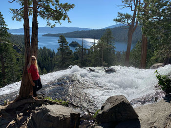 Front view of woman leaning against tree by lake and waterfall