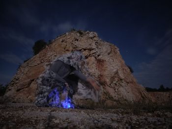 Man crouching by rock formations against sky at night