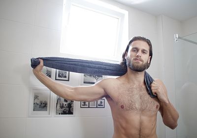 Portrait of shirtless young man standing at domestic bathroom