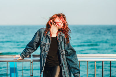 Smiling young woman with tousled hair standing by railing against sea