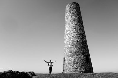 Woman standing by built structure on field against clear sky