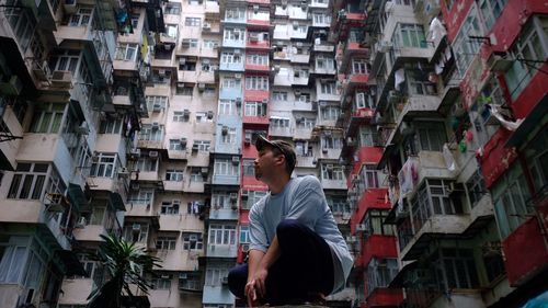 Low angle view of man sitting against buildings in city