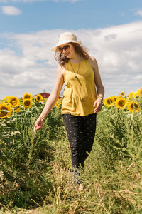 Rear view of woman standing amidst plants on field against sky