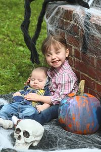 Smiling girl with baby boy sitting by pumpkin during halloween