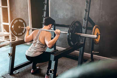 Rear view of man exercising with barbell at gym