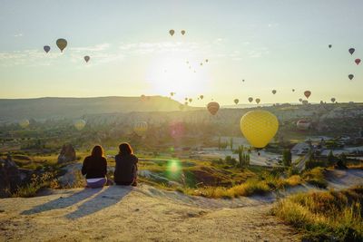 Women looking at hot air balloons while sitting on mountain at cappadocia