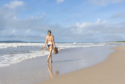 Woman in bikini walking on beach sand against blue sky. 