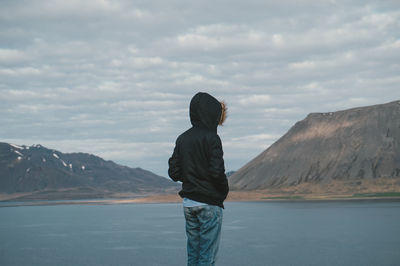 Rear view of man standing in front of sea against cloudy sky