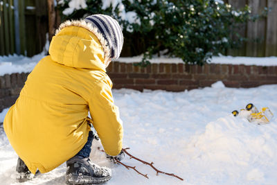 Little boy plays with snow in the backyard.