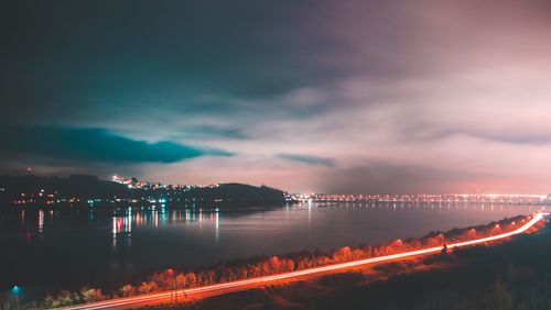 Illuminated city by sea against sky at night