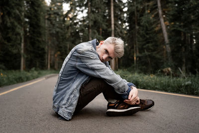 Side view portrait of man sitting on road in forest