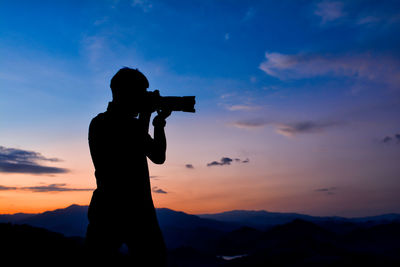 Side view of silhouette man photographing against sky during sunset