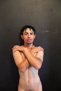 Portrait of shirtless man standing against wall