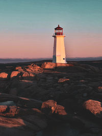 Lighthouse by sea against sky during sunset