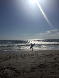 Silhouette man standing on beach against sky on sunny day