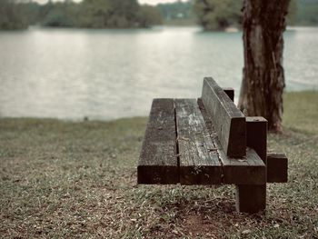 Wooden bench on field by lake