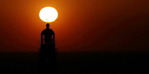 Silhouette lighthouse by sea against sky during sunset