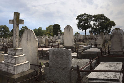 Cross and tombstones at cemetery against sky